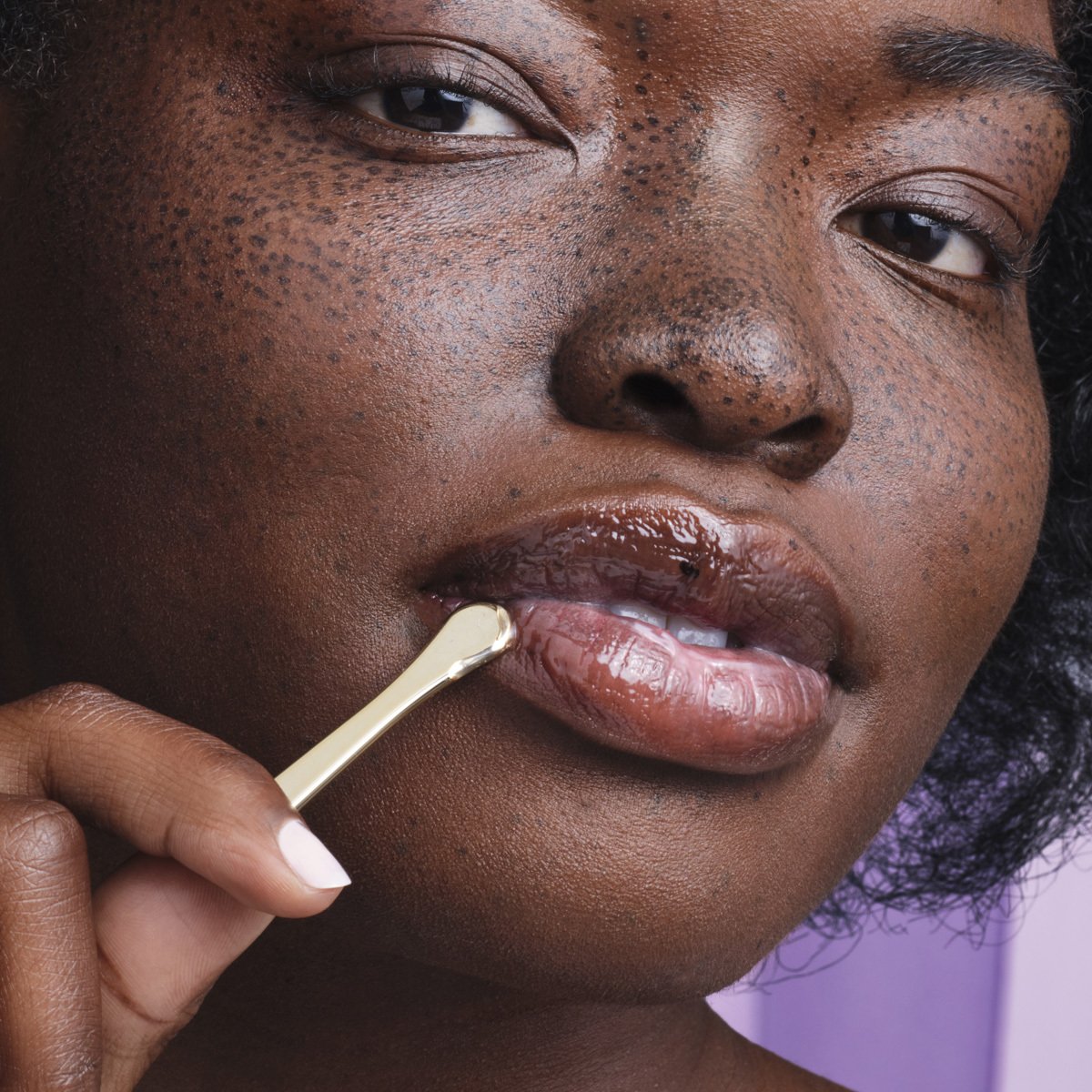 Model applying The Kissu Lip Mask on lips with gold spoon applicator.