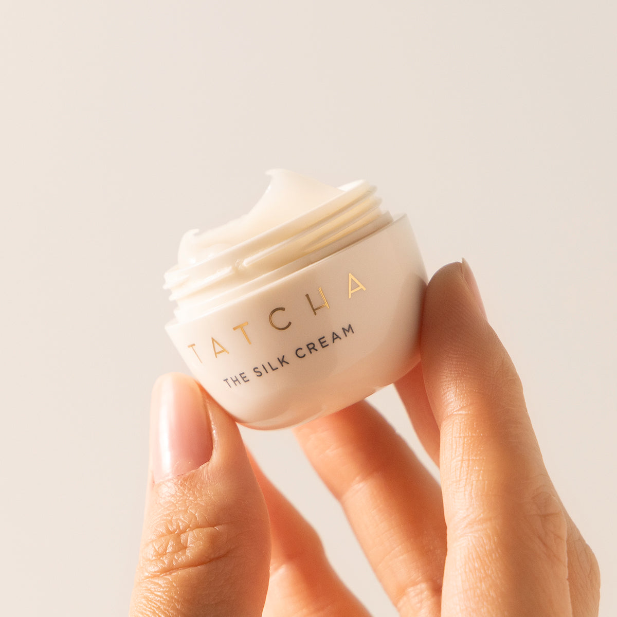 Hand holding a jar of Tatcha The Silk Cream against a neutral background