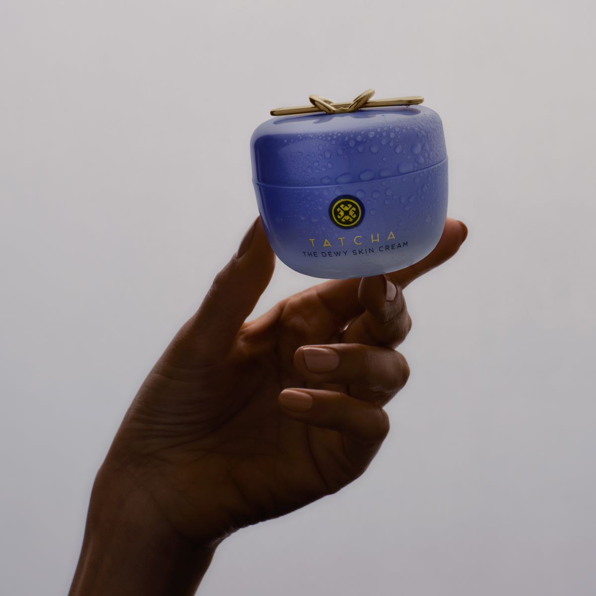 A hand holding the Tatcha Dewy Skin Cream