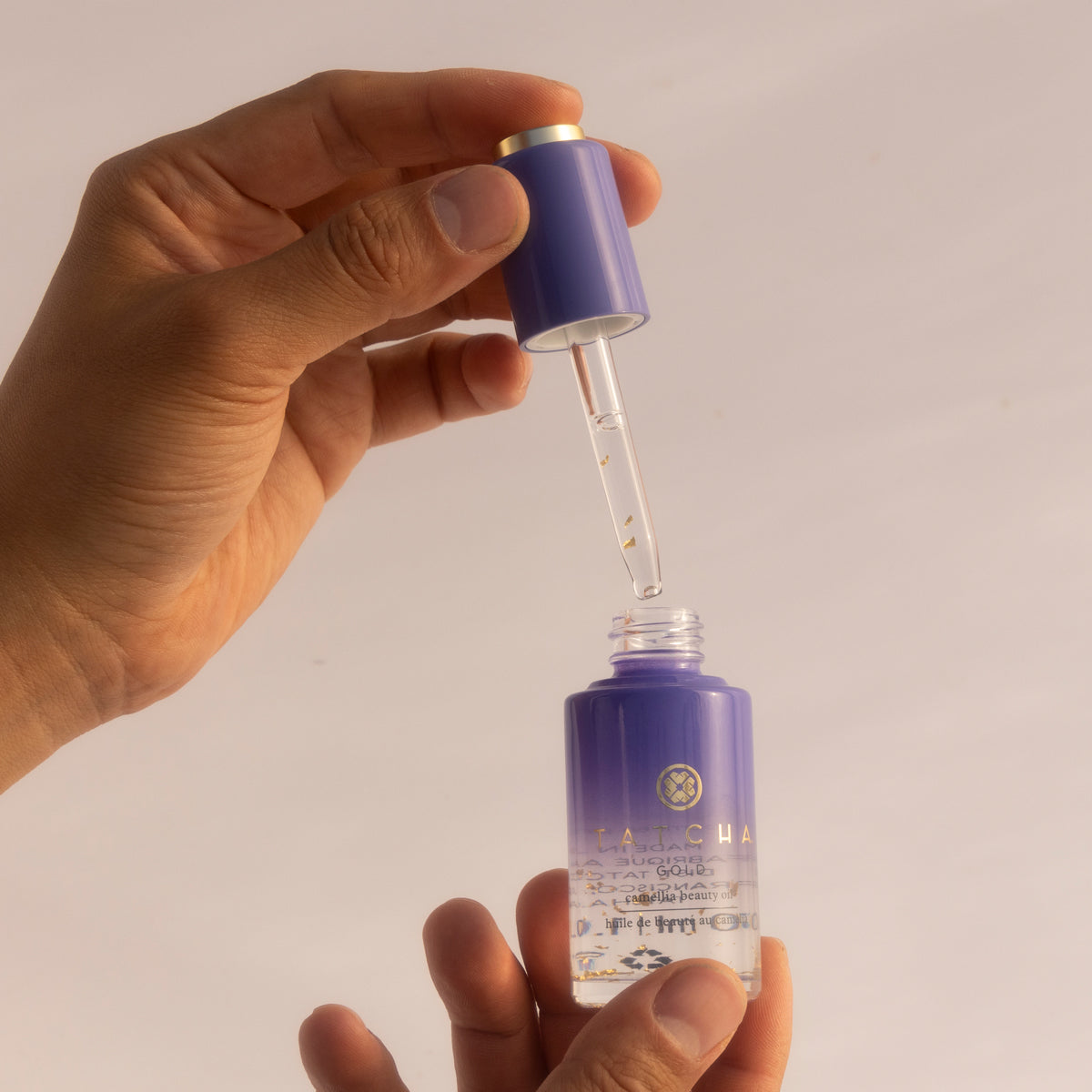 Hand holding a purple dropper bottle with a camellia oil
