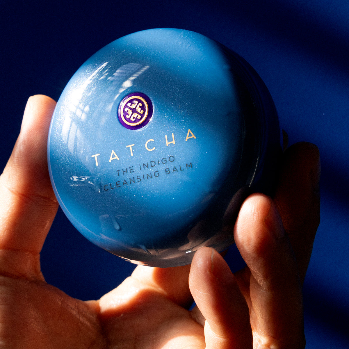 Tatcha The Indigo Cleansing Balm held in a hand against a dark background