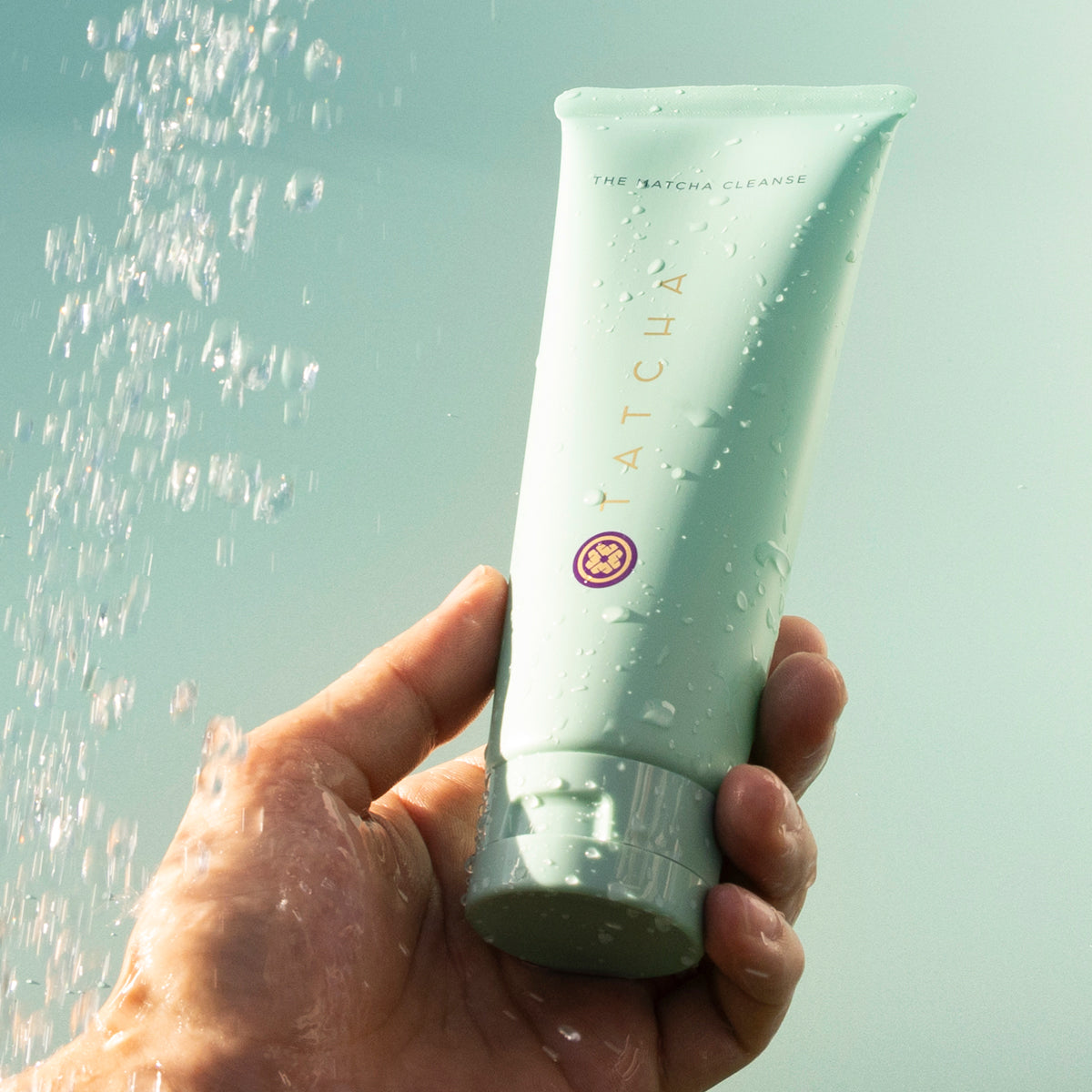 Hand holding The Matcha Cleanse under a shower of warter